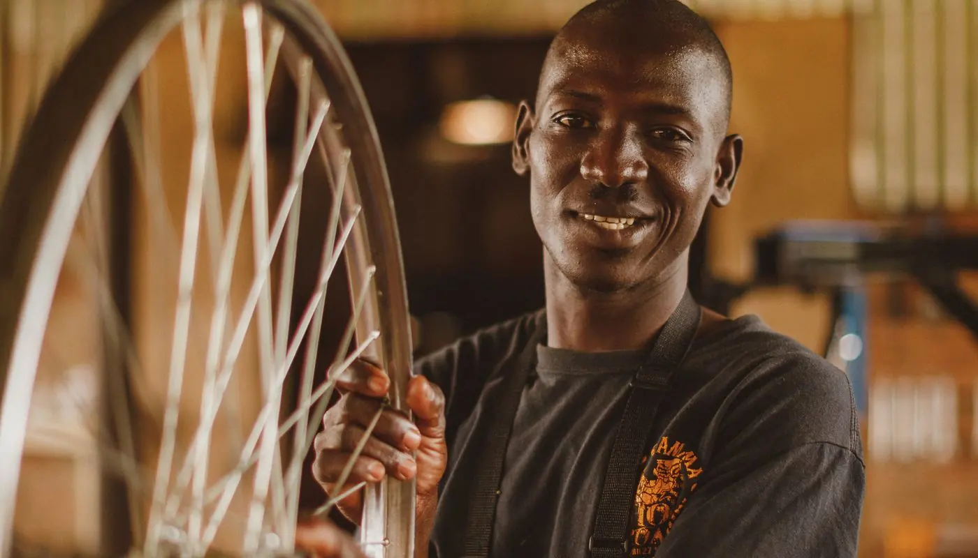 Un artisan souriant dans son atelier, une roue de vélo entre les mains.